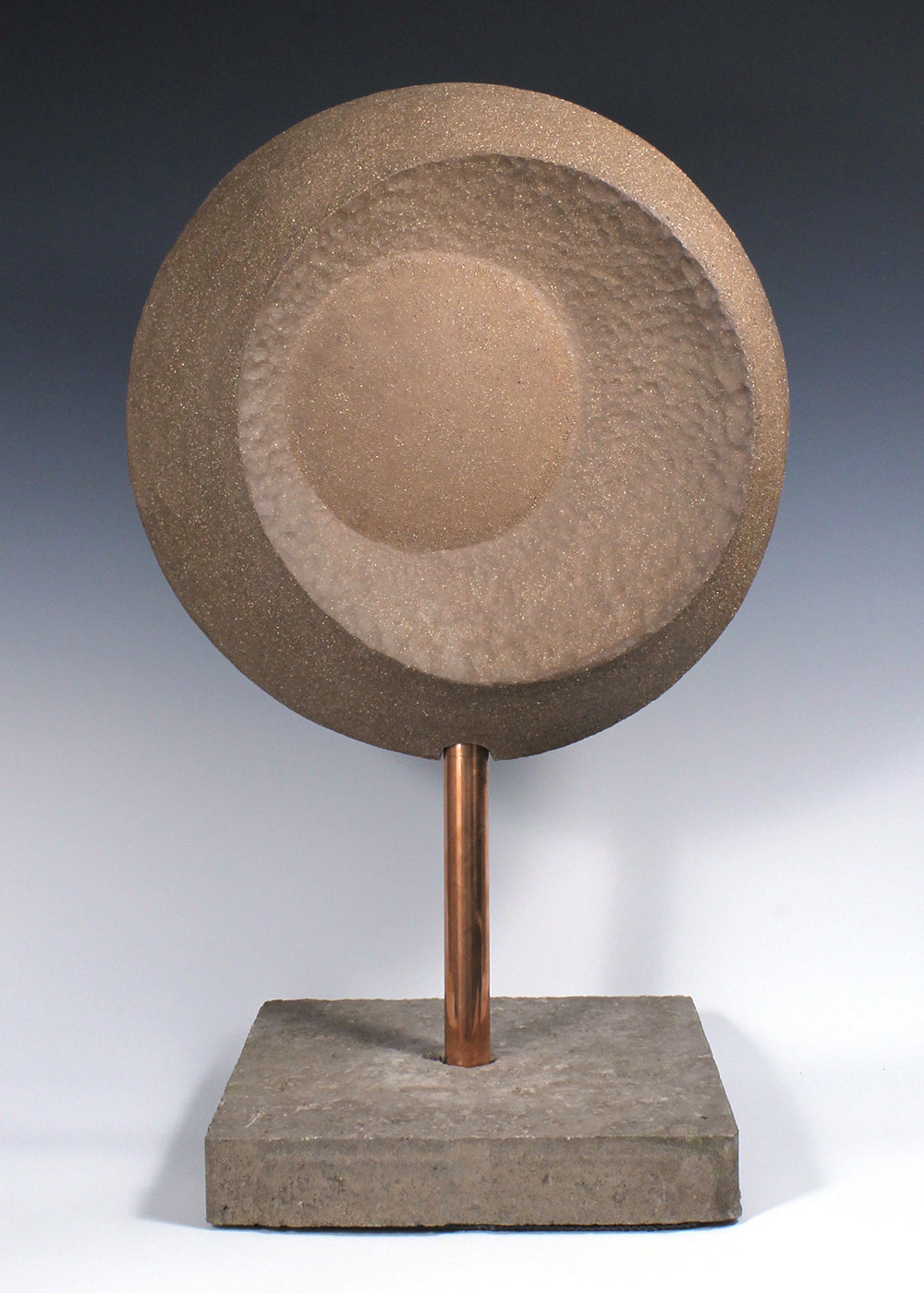 Large circular ceramic sculpture with convex and concave surfaces mounted on custom base with copper piping through a concrete base